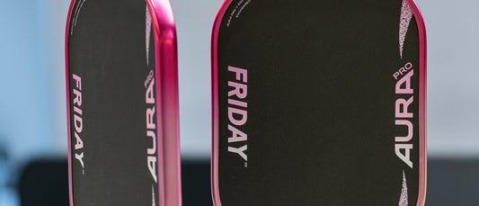Two Friday Aura Pro Elongated Metallic Pink Prism paddles, with pink grips, in front of a Dinklab sign.