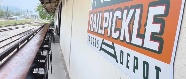 The Rail Pickle Sports Depot sign, with the railway line running alongside the courtside seating.