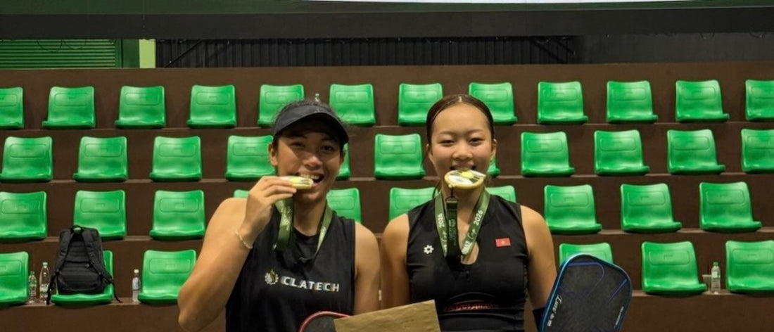 Tya Karina (left) and Sophia Tran Phuong Anh (right) bite their gold medals in front of the Tomaz Cup Gold Medal Match screen.