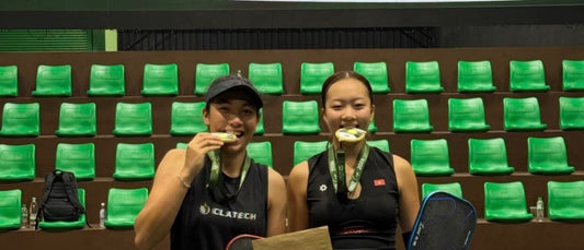 Tya Karina (left) and Sophia Tran Phuong Anh (right) bite their gold medals in front of the Tomaz Cup Gold Medal Match screen.